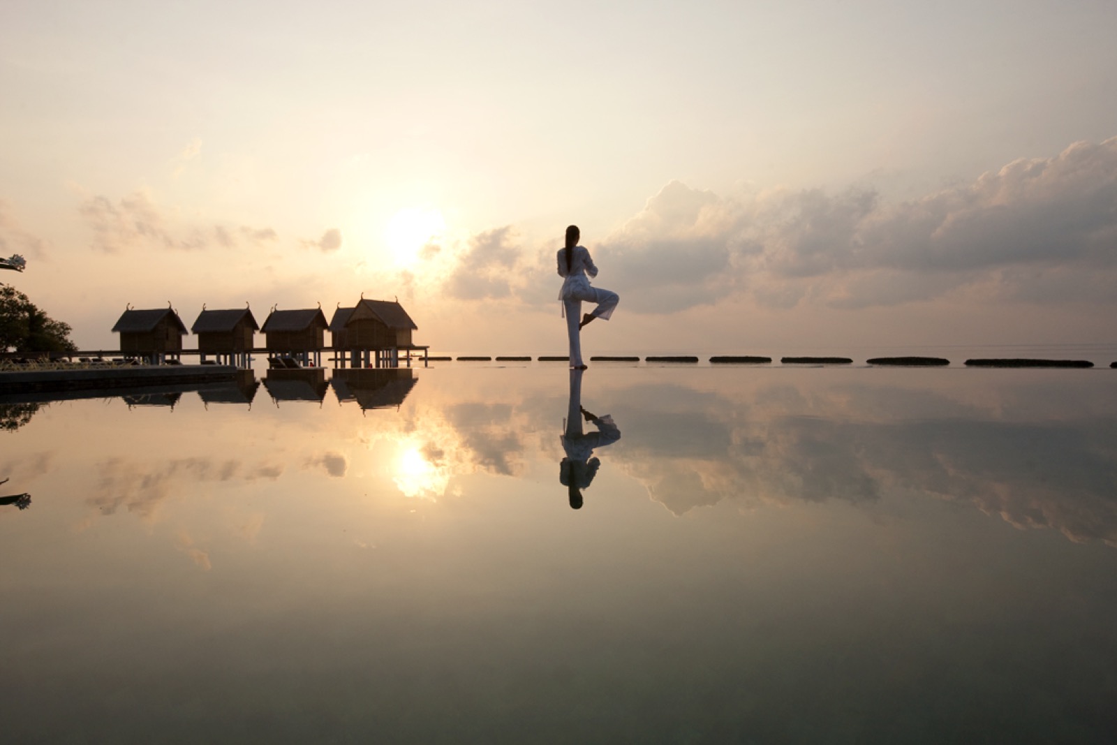 Silhouette d'une femme en posture de yoga au bord d'une piscine à débordement