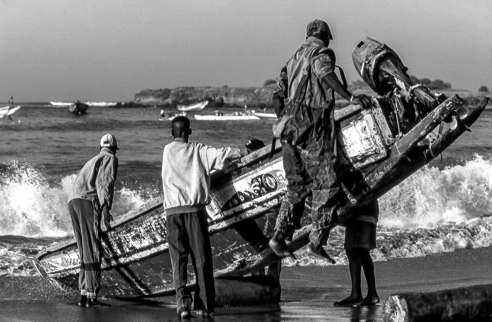 Pêcheurs hissant une pirogue dans l'écume, Sénégal, photographie en noir et blanc