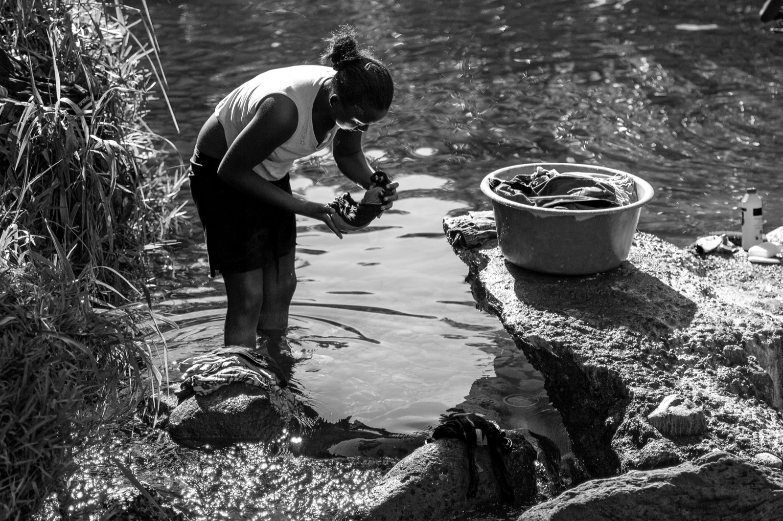 Femme lavant du linge à la rivière près d'une bassine émaillée, photographie en noir et blanc