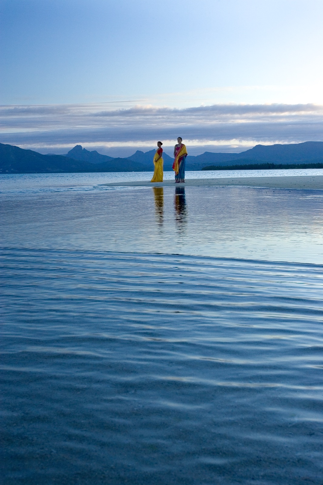 Deux femmes en saris colorés sur un banc de sable au bord d'un lagon à l'aube