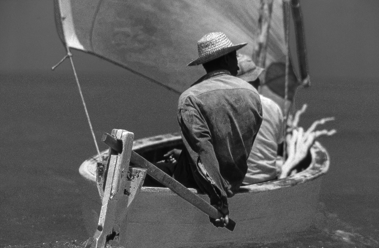 Pêcheur en chapeau de paille ramant dans une pirogue à voile, photographie en noir et blanc